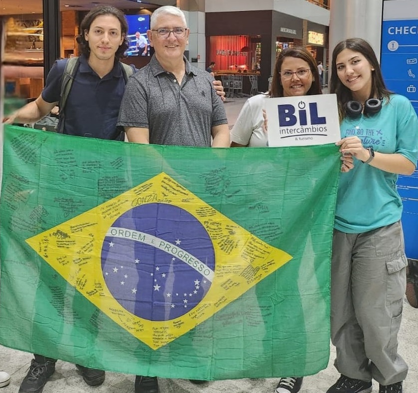 Estudante com os pais no aeroporto segurando a bandeira do Brasil. 